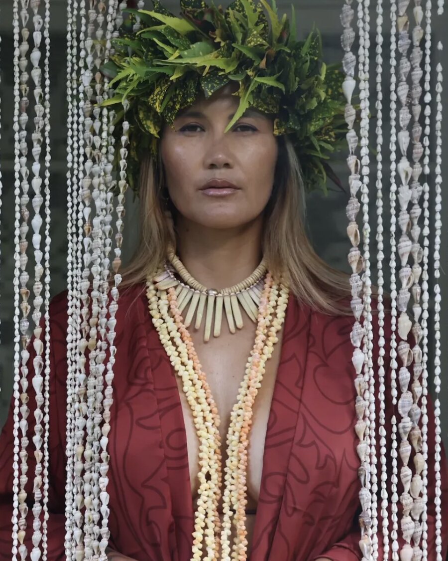 Callie Moasen wearing a crown of leaves and shell necklaces, between garlands of shells